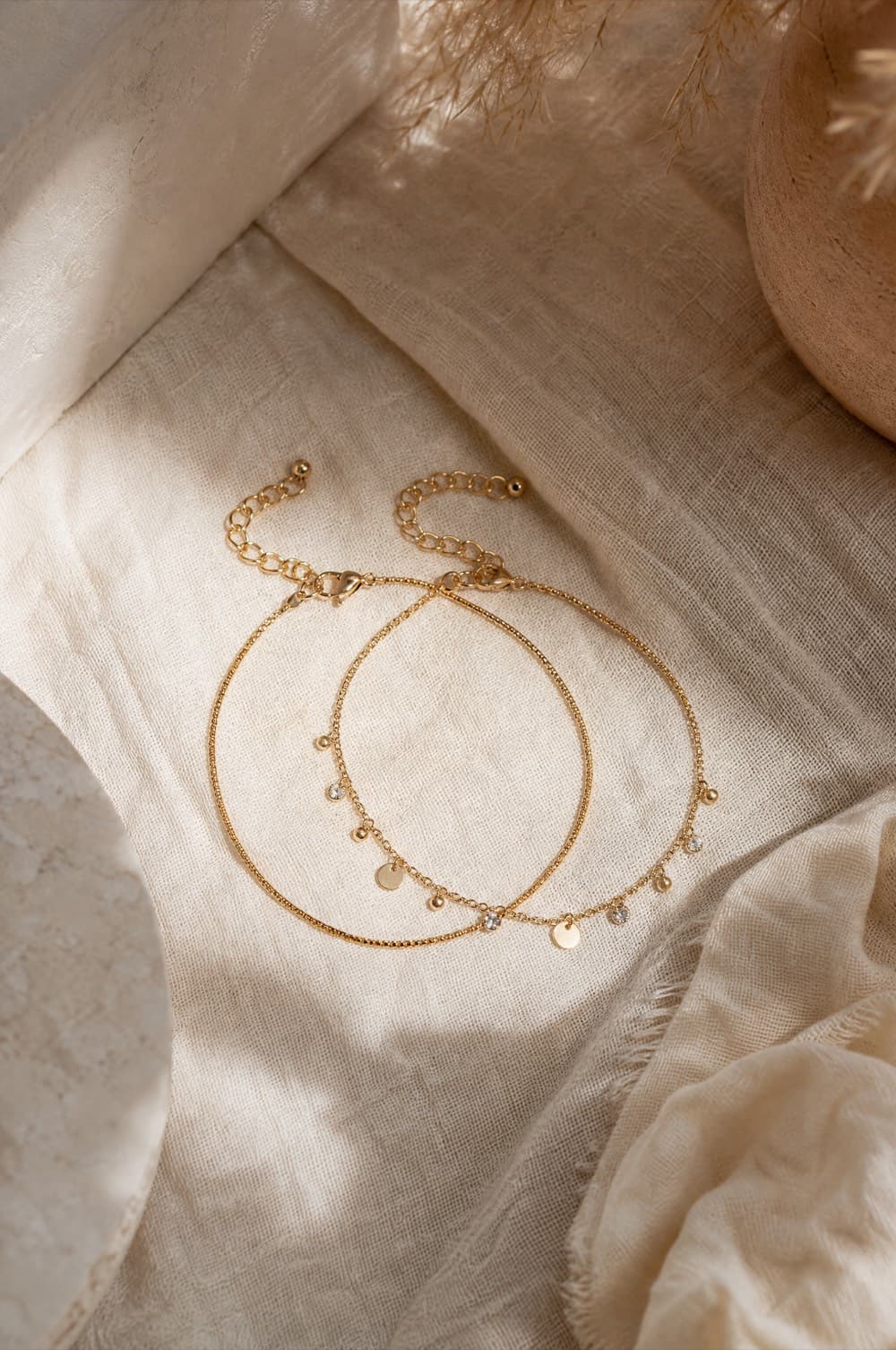 Two fine gold-tone anklets, one plain and one with small charms