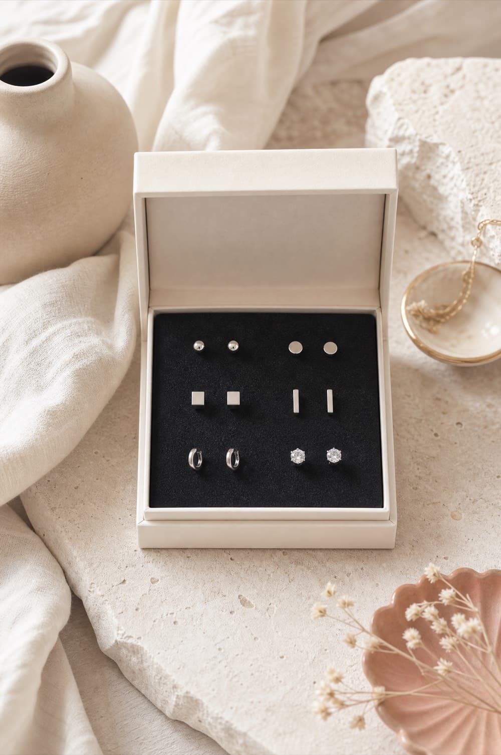 Six pairs of small stainless steel stud earrings in a foam insert box