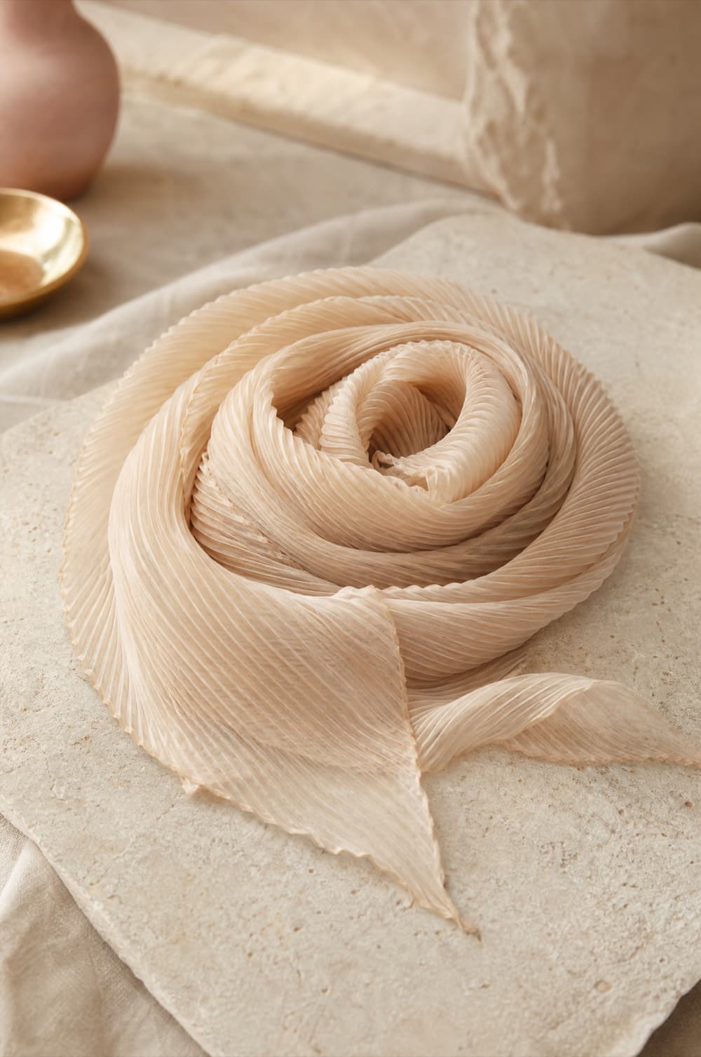 Finely pleated chiffon scarf coiled on a champagne backdrop
