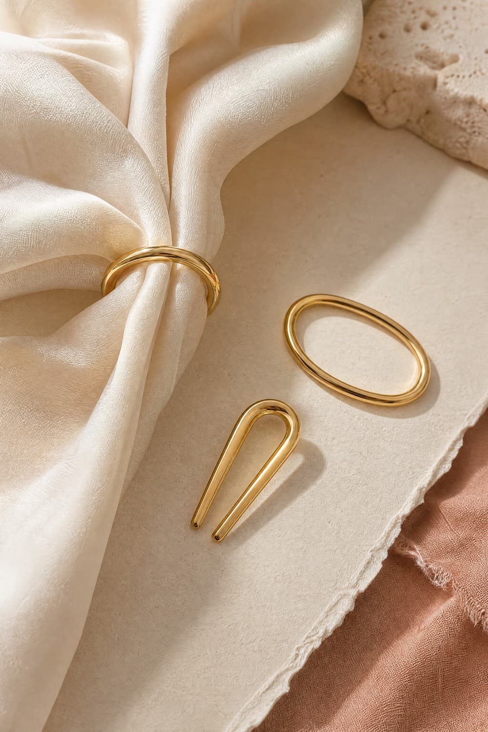 Two gold-tone scarf rings and a shaping clip on a linen surface