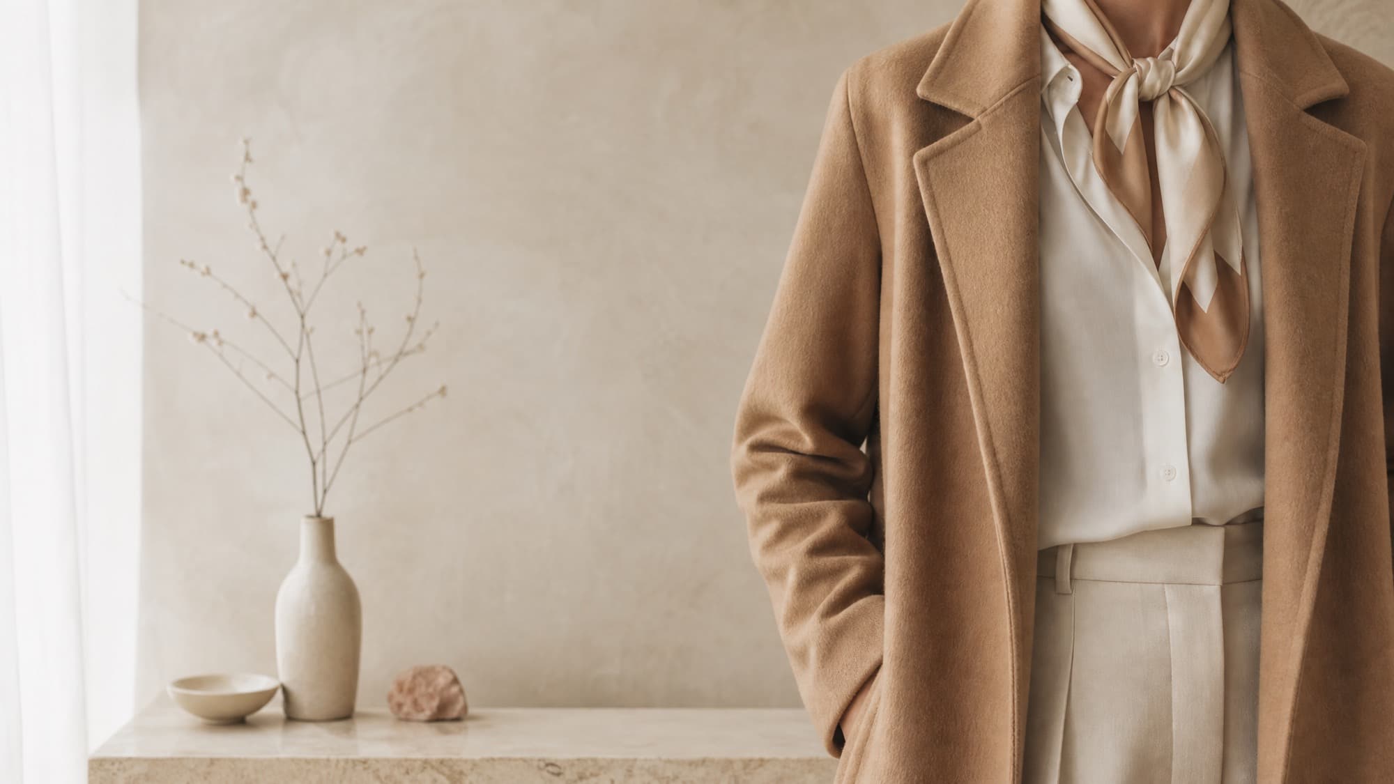 A camel coat worn over an ivory shirt with a small silk-feel scarf knotted at the collar