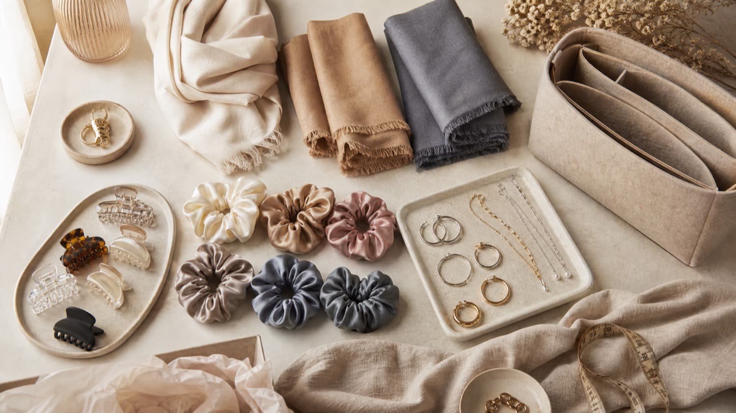An accessories styling table with folded scarves, hair clips, hoops and fine chains
