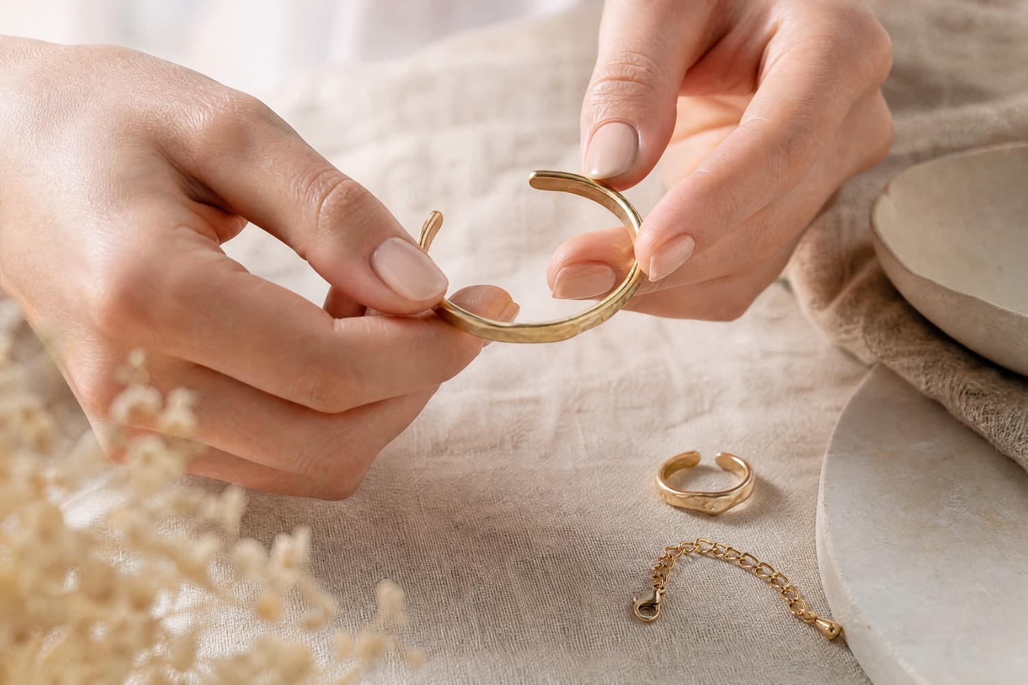 Hands gently opening an adjustable cuff bracelet beside an open ring and a chain extender
